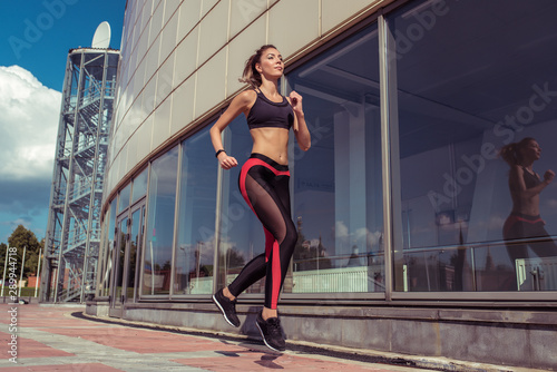 Sports beautiful girl in summer runs jogging, sportswear top leggings, morning bright sunny day. Active lifestyle, fitness motivation workout. In movement, a woman is strong and hardy.