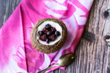 Berry dessert with yogurt in a cup of coconut on a wooden background. Blackberries, raspberries, blueberries, black currants. Pink napkin