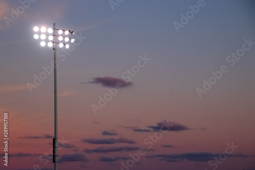 Stadium night lights over football field during sunset with cumulous clouds