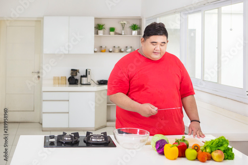 Overweight man holding a knife in the kitchen