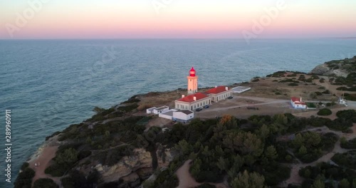 Farol de Alfanzina, Aerial, tracking, drone shot, panning towards the Carvoeiro lighthouse, on the coast of South Algarve, at the Atlantic sea, at sunrise, on a sunny morning, in Lagos, Portugal photo