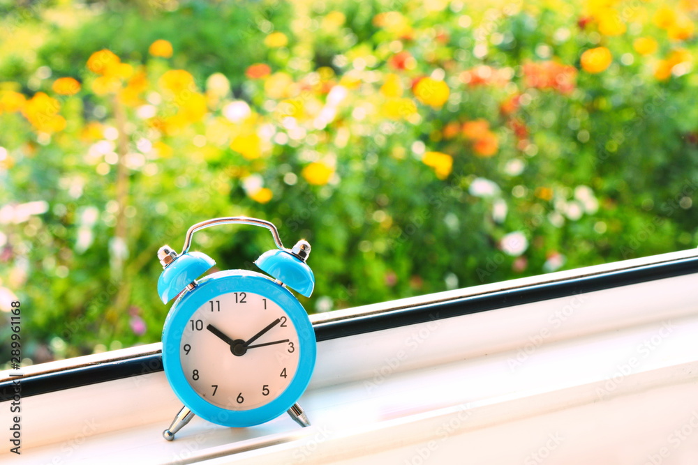 Blue retro classic alarm clock the hands on the dial show the morning time  on window with bright blurred flower background behind glass. Summer  sunrise beautiful wallpaper Photos | Adobe Stock