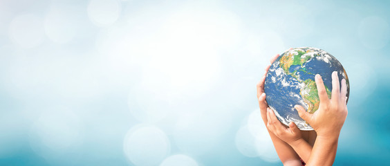 Earth Day concept with many hands holding globe together for world unity and environmental protection on blue nature background with bokeh and copy space for global conservation