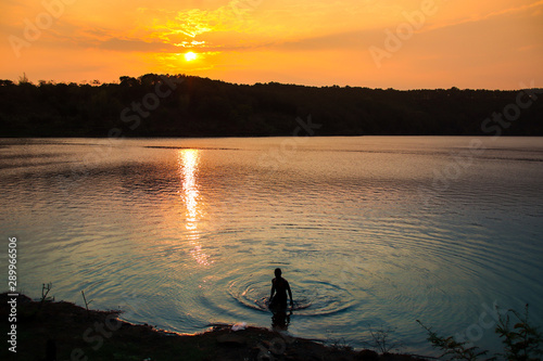 Silhouette of a person taking a relaxing and soothing bath on a lake against the sunset