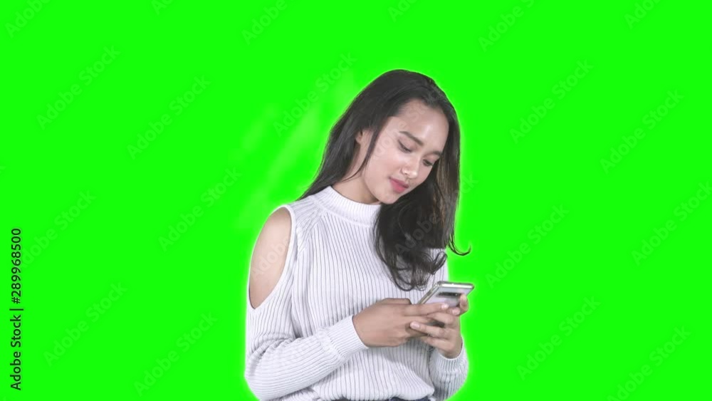 Beautiful teenage girl standing in the studio while using a mobile phone. Shot in 4k resolution with green screen background Beautiful teenage girl standing in the studio while using a mobile phone. Shot in 4k resolution with green screen background