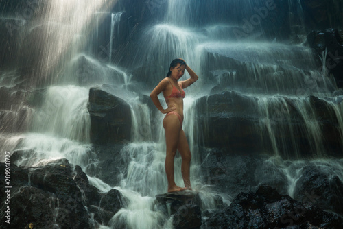 natural portrait of young beautiful and happy Asian Chinese woman in bikini enjoying nature at tropical paradise waterfall with magical feeling in soul inspiration