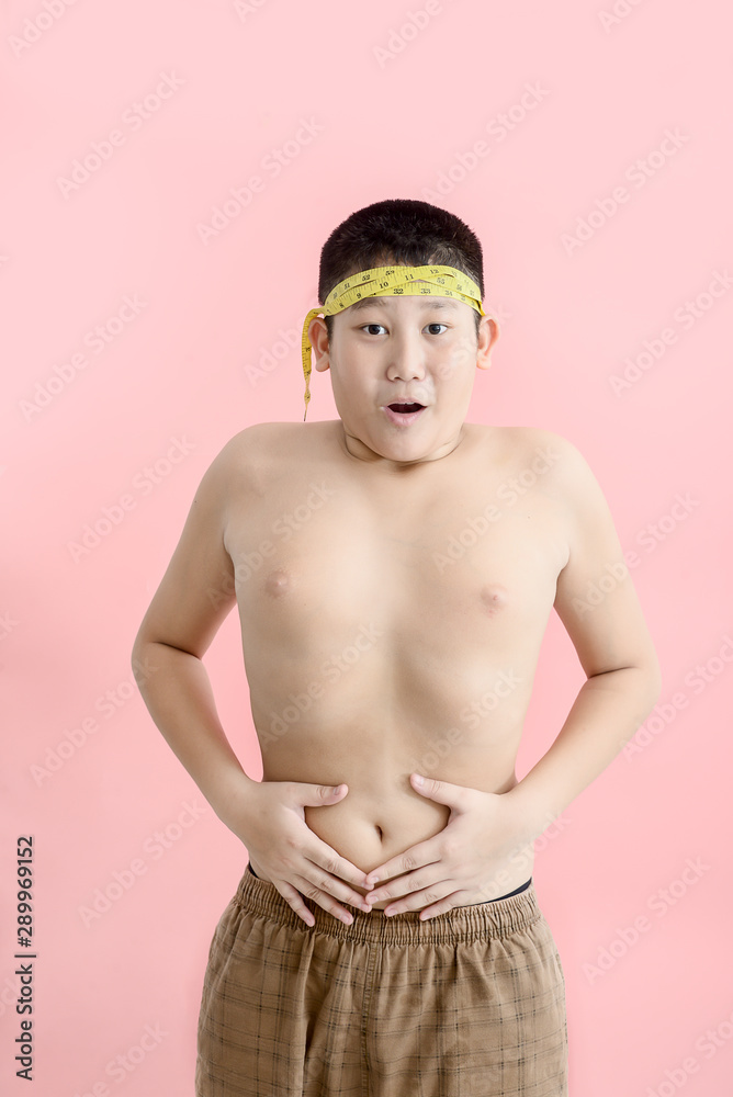 Asian boy with his belly with a tape measure on a pink background, concept fat boy, unhealthy