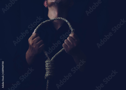 Foto Close up of a sad man holding rope with hangman's noose in the dark room  while