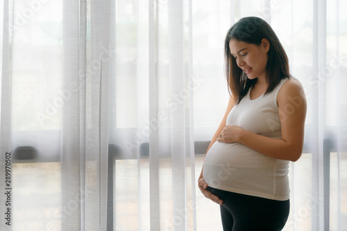 Pregnant asian woman standing near the window. © thepoo