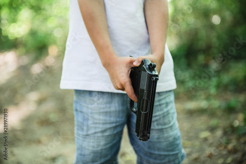 american little boy in white shirt holding black gun weapon in hands get ready to shoot in outdoor parkland