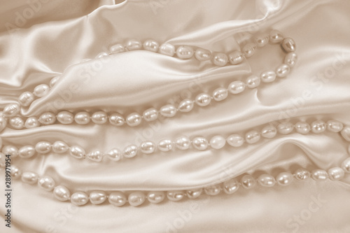 Delicate beige satin draped fabric with natural river pearls for festive backgrounds