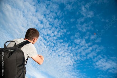 active healthy young caucasian man with backpack control flying kite in blue cloud sunset summer sky