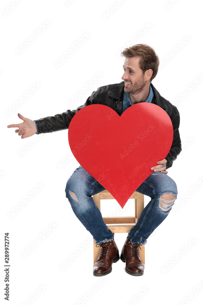 seated man holding a heart pointing to a side seated man holding a heart pointing to a side