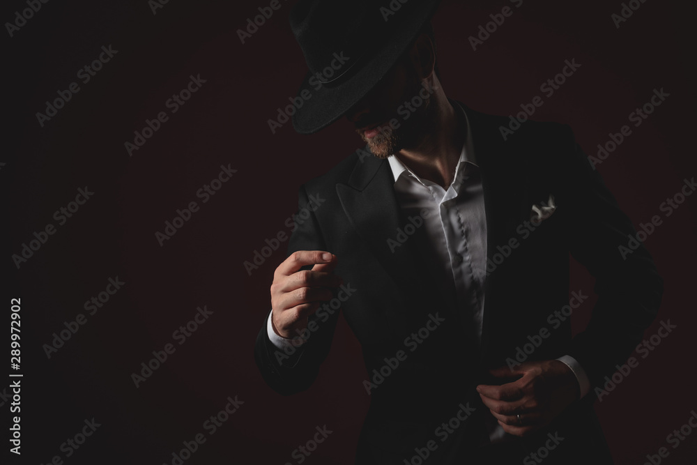 mysterious young man fixing coat on black background