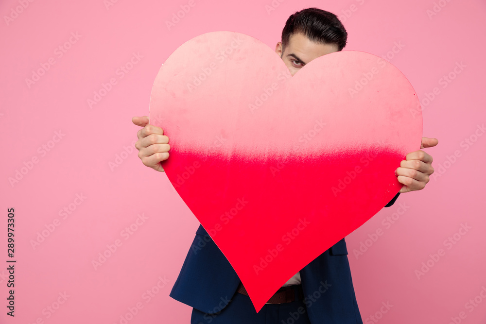 attractive young man holding a big heart on pink background attractive young man holding a big heart on pink background