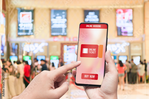 Mockup mobile phone hand using smartphone to buy cinema tickets with blurred image of ticket sales counter at movie theater with graphic icon, online booking and payment concept