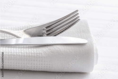 Silver fork and knife with napkin on white table cloth.Restaurant dinning concept background