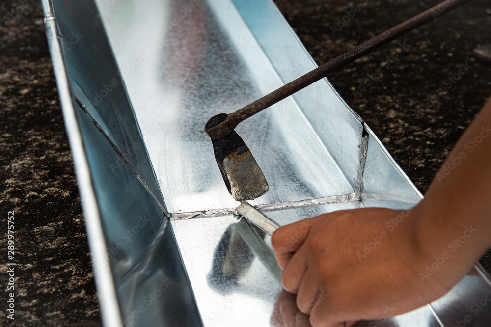 Closeup hand using old fashioned bonding to solder aluminium gutter roof. Stock Photo Adobe Stock