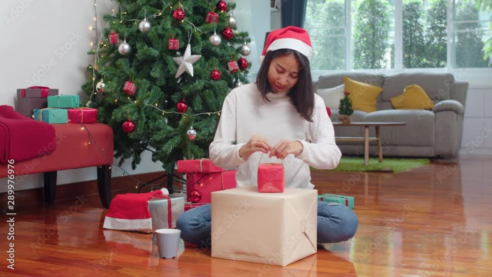 Asian women celebrate Christmas festival. Female teen wear sweater and Christmas hat relax happy wrapping gifts near Christmas tree enjoy xmas winter holidays together in living room at home. Asian women celebrate Christmas festival. Female teen wear sweater and Christmas hat relax happy wrapping gifts near Christmas tree enjoy xmas winter holidays together in living room at home.