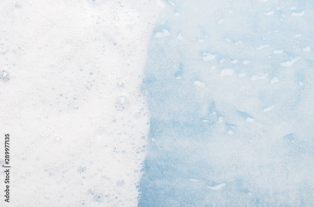 Obraz premium White foam on blue water top view background. Soapy liquid with white bubbles macro. Mousse texture, snow-white froth. Shower gel foam closeup. Household washing liquid, detergent dissolving in water
