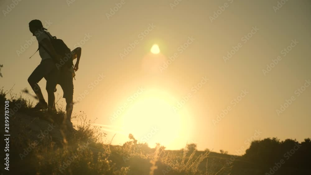 Teamwork. Silhouette of children holding out a helping hand. Two boys tourists on top of the mountain. Children help each other climb a steep stone Teamwork. Silhouette of children holding out a helping hand. Two boys tourists on top of the mountain. Children help each other climb a steep stone