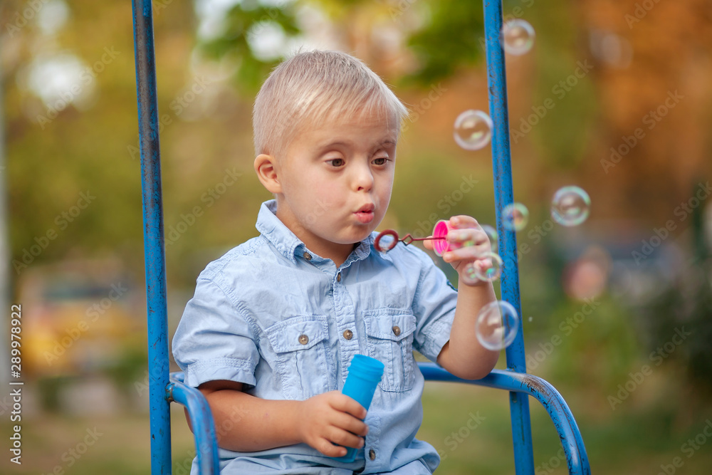 Φωτογραφία Boy with Down syndrome blowing soap bubbles, cute European child with a genetic abnormality, disabled children, extra chromosome, psychiatric illness in children