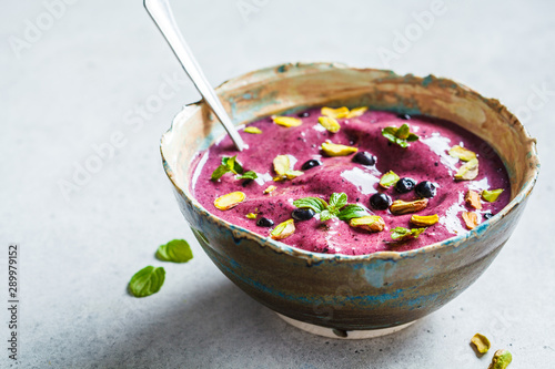 Blueberry smoothie bowl with pistachios and mint on white background. Healthy vegan breakfast.