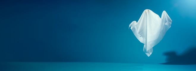 Photo of halloween ghosts made of white fabric on empty blue background.