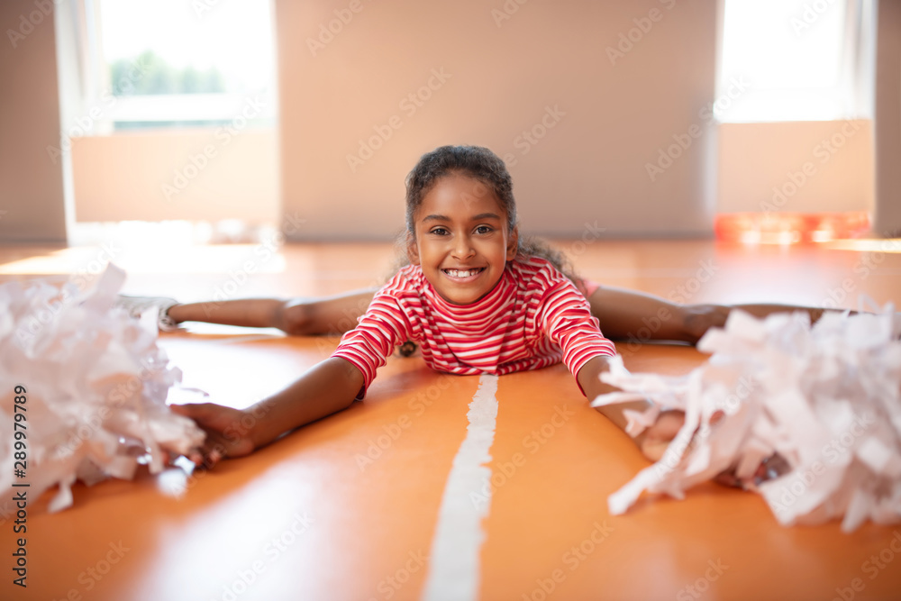 Fototapeta premium Little beaming cheerleader feeling happy while splitting legs