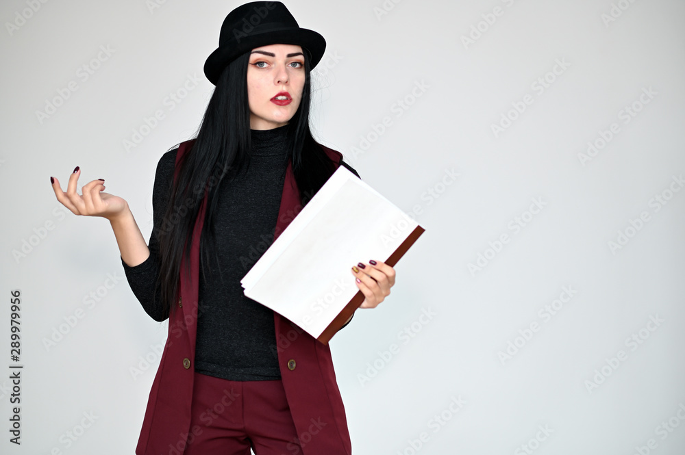 Concept portrait of a pretty brunette girl with long black hair in a hat and a business suit on a white background in studio. Standing right in front of the camera in various poses. Concept portrait of a pretty brunette girl with long black hair in a hat and a business suit on a white background in studio. Standing right in front of the camera in various poses.