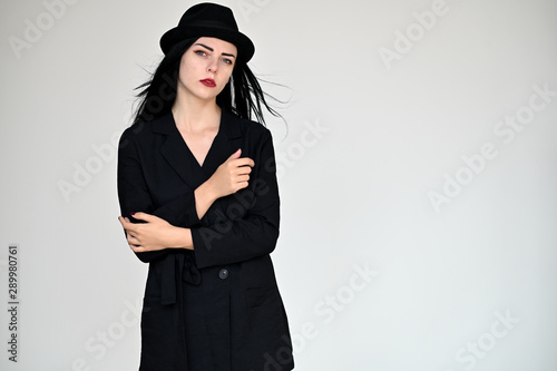 Concept portrait of a pretty brunette girl with long black hair in a hat and a business suit on a white background in studio. Standing right in front of the camera in various poses. © Вячеслав Чичаев