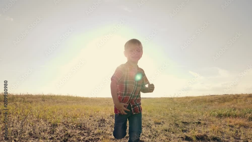 Happy boy runs on a green field in the sun at sunset. Children's games, travel dreams. Concept of childish happiness Happy boy runs on a green field in the sun at sunset. Children's games, travel dreams. Concept of childish happiness