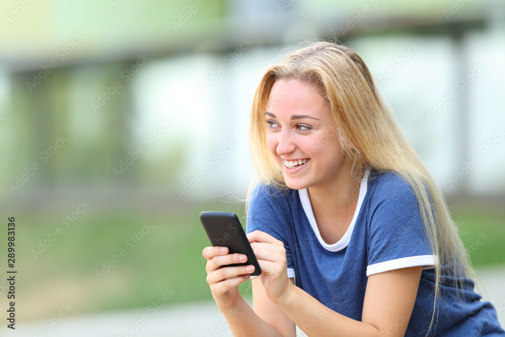 Happy teenage girl holding phone looking at side Happy teenage girl holding phone looking at side