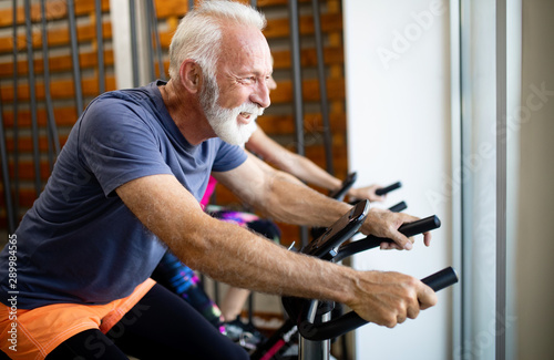 Happy fit mature woman and man cycling on exercise bikes to stay healthy