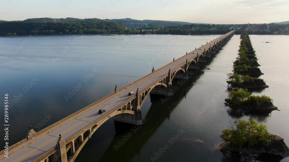 Dolly forward drone shot of Susquehanna River at sunset with traffic, old bridge piers remain after bridge burned in US Civil War Dolly forward drone shot of Susquehanna River at sunset with traffic, old bridge piers remain after bridge burned in US Civil War