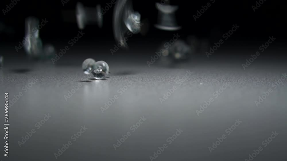 Clear push pin tacks fall on gray and white table two pins touch in slow motion shallow depth