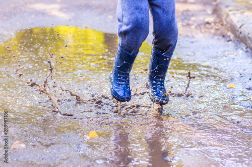 A little boy is jumping in a puddle. A boy in rubber boots. Happy childhood. Puddles after the rain. Warm summer evening.