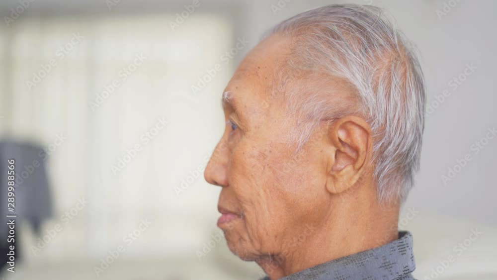 Side view of senior man with wrinkled skin and gray hair sitting in the living room at home. Shot in 4k resolution