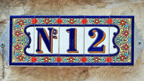Number 12, twelve, house number decorative ceramic tile digit on a grunge stone wall.