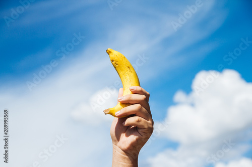 Banana in hand across blue sky background, concept diet for good healthy