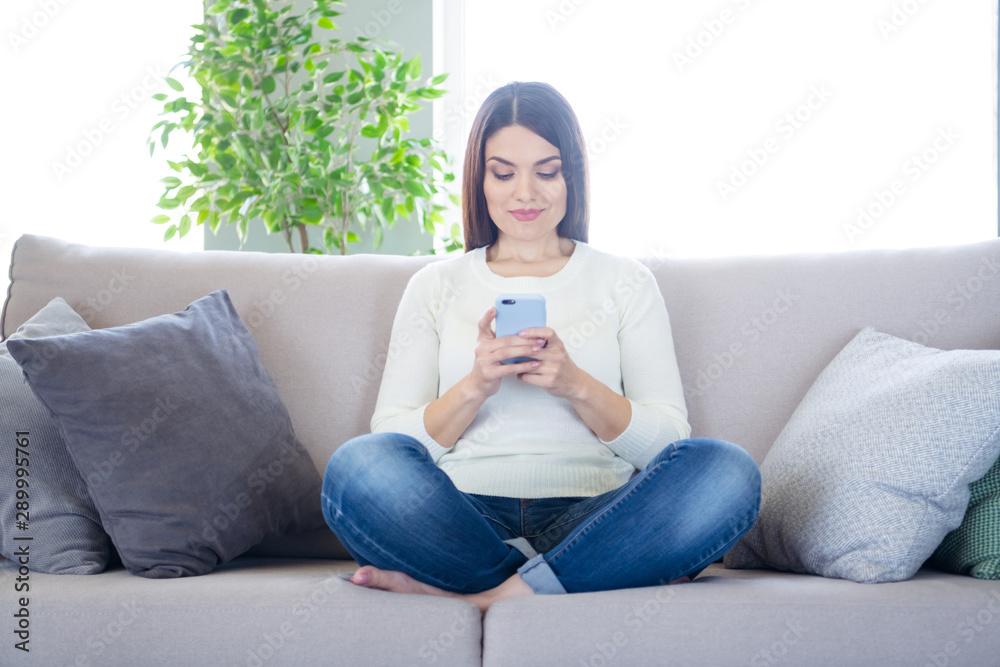 Portrait of her she nice attractive charming lovely peaceful focused woman sitting in lotus position on cosy divan using wi-fi wireless connection in light white interior living-room indoors Portrait of her she nice attractive charming lovely peaceful focused woman sitting in lotus position on cosy divan using wi-fi wireless connection in light white interior living-room indoors