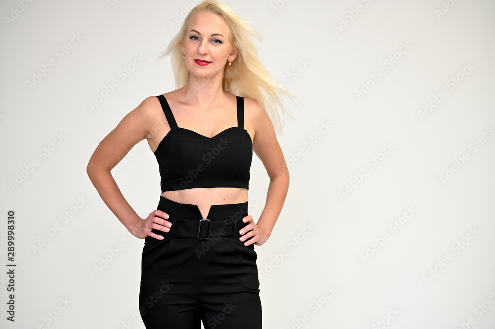 Concept portrait of a pretty young blonde woman with long beautiful hair in a black suit on a white background in studio. Standing in front of the camera in various poses with a smile. Concept portrait of a pretty young blonde woman with long beautiful hair in a black suit on a white background in studio. Standing in front of the camera in various poses with a smile.