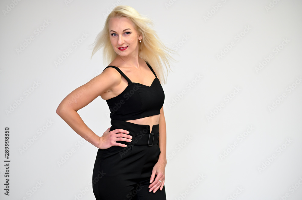 Concept portrait of a pretty young blonde woman with long beautiful hair in a black suit on a white background in studio. Standing in front of the camera in various poses with a smile. Concept portrait of a pretty young blonde woman with long beautiful hair in a black suit on a white background in studio. Standing in front of the camera in various poses with a smile.