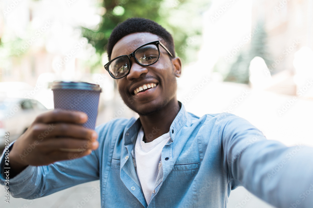Cheerful young african guy standing outdoors holding coffee make selfie by camera. Cheerful young african guy standing outdoors holding coffee make selfie by camera.