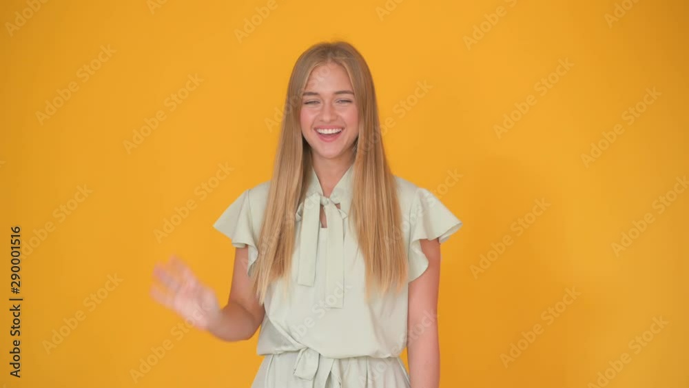 happy beautiful blonde girl waving hello and smiling isolated over yellow happy beautiful blonde girl waving hello and smiling isolated over yellow
