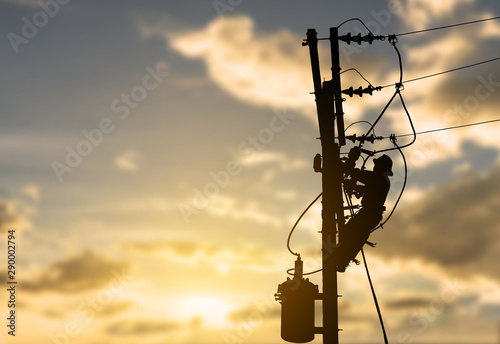 Silhouette electrician working maintenance equipment on  electric pole in sunset background.