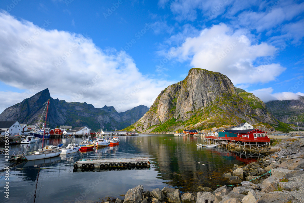A fishing village at Hamnoy Reine, Norway during the daytime. The blue skies and mountains reflect the water.