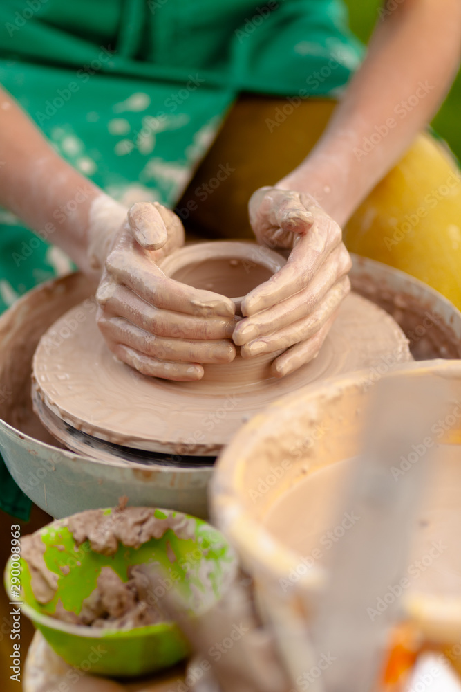 Hand craft making pottery on wheel. Female hands mold ceramic plate from clay (pot).