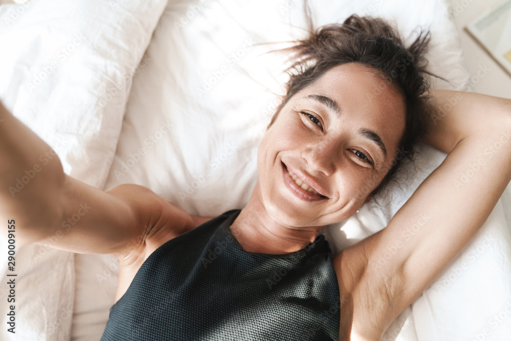 Pretty cute beautiful woman indoors at home on bed take a selfie by camera. Pretty cute beautiful woman indoors at home on bed take a selfie by camera.