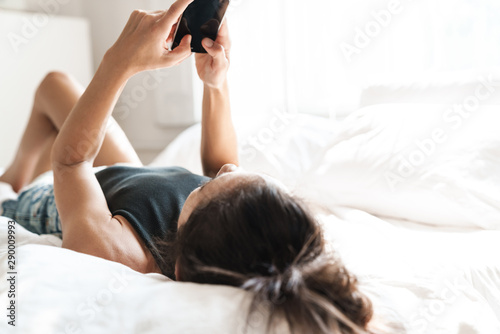Beautiful woman indoors at home on bed using mobile phone.